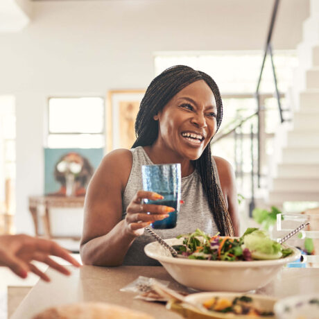 femme tient un verre d'eau devant une assiette de salade
