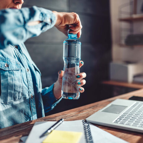 femme ouvrant sa gourde d'eau devant bureau